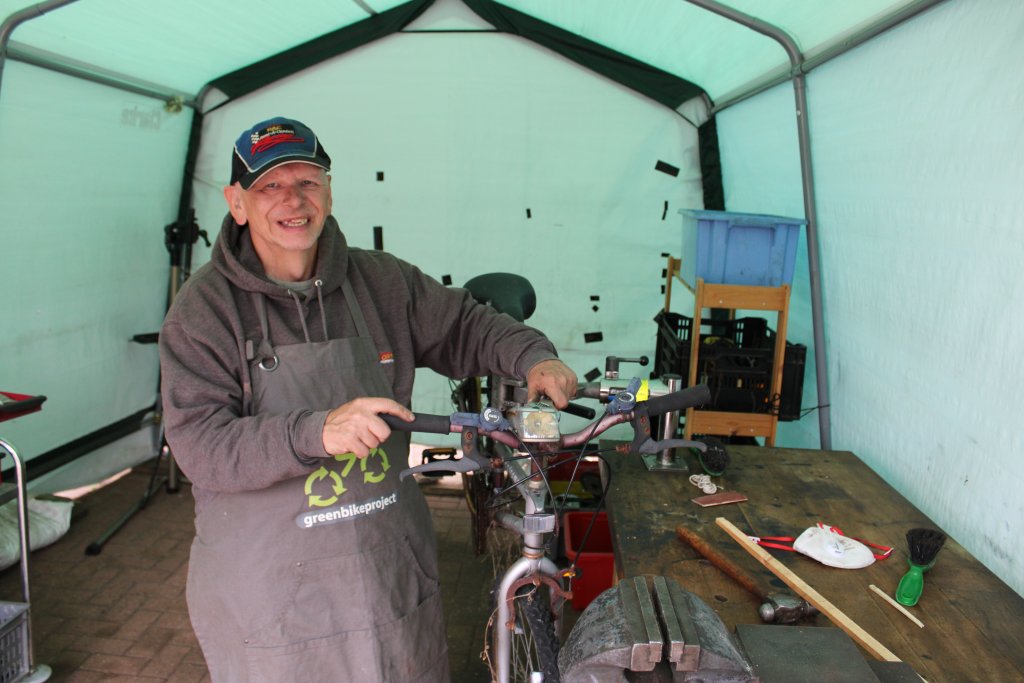 Genesis Orwell Mencap service user, Simon Pratt, standing next to a bicycle he is repairing.